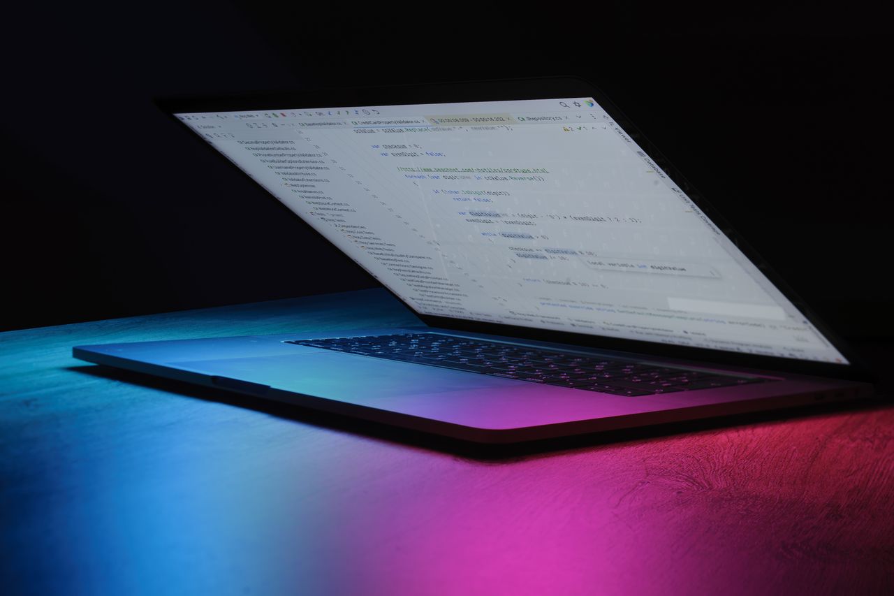 hero-img A partially open laptop displaying code, bathed in vibrant neon lighting.